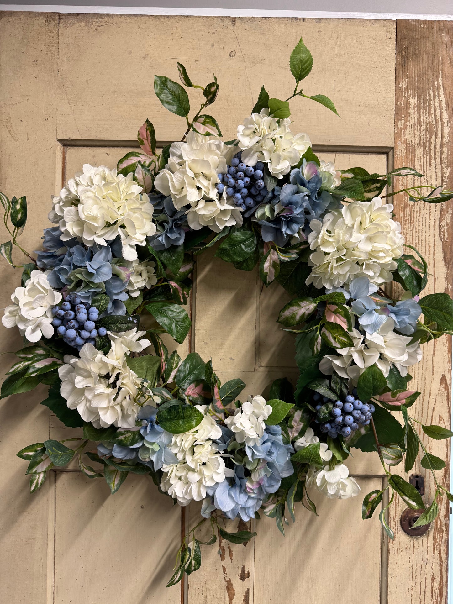 Handmade coastal hydrangea wreath with white and soft blue hydrangeas, blueberry clusters, and variegated Hoya greenery on an 18-inch grapevine base"