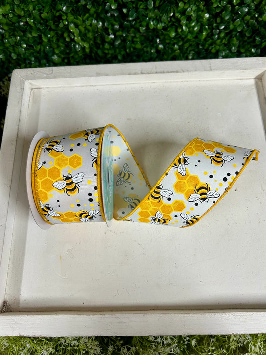 2.5 inch wired white ribbon with bumblebee and honeycomb print in yellow and black, rolled on a white decorative tray with green boxwood backdrop