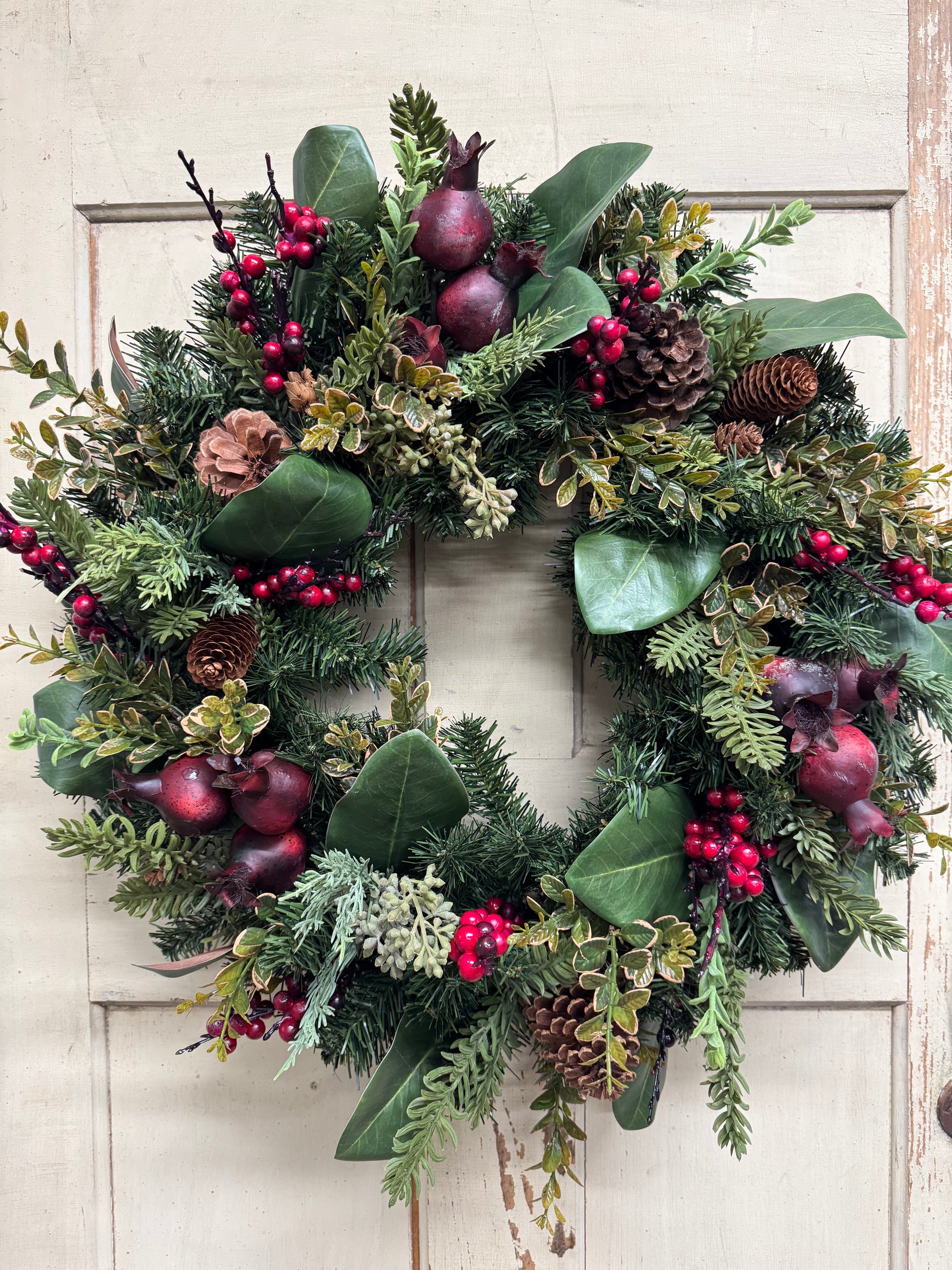 Christmas wreath with burgundy pomegranates, red berries, pinecones, mixed pine greenery, magnolia leaves, and green and gold boxwood.”