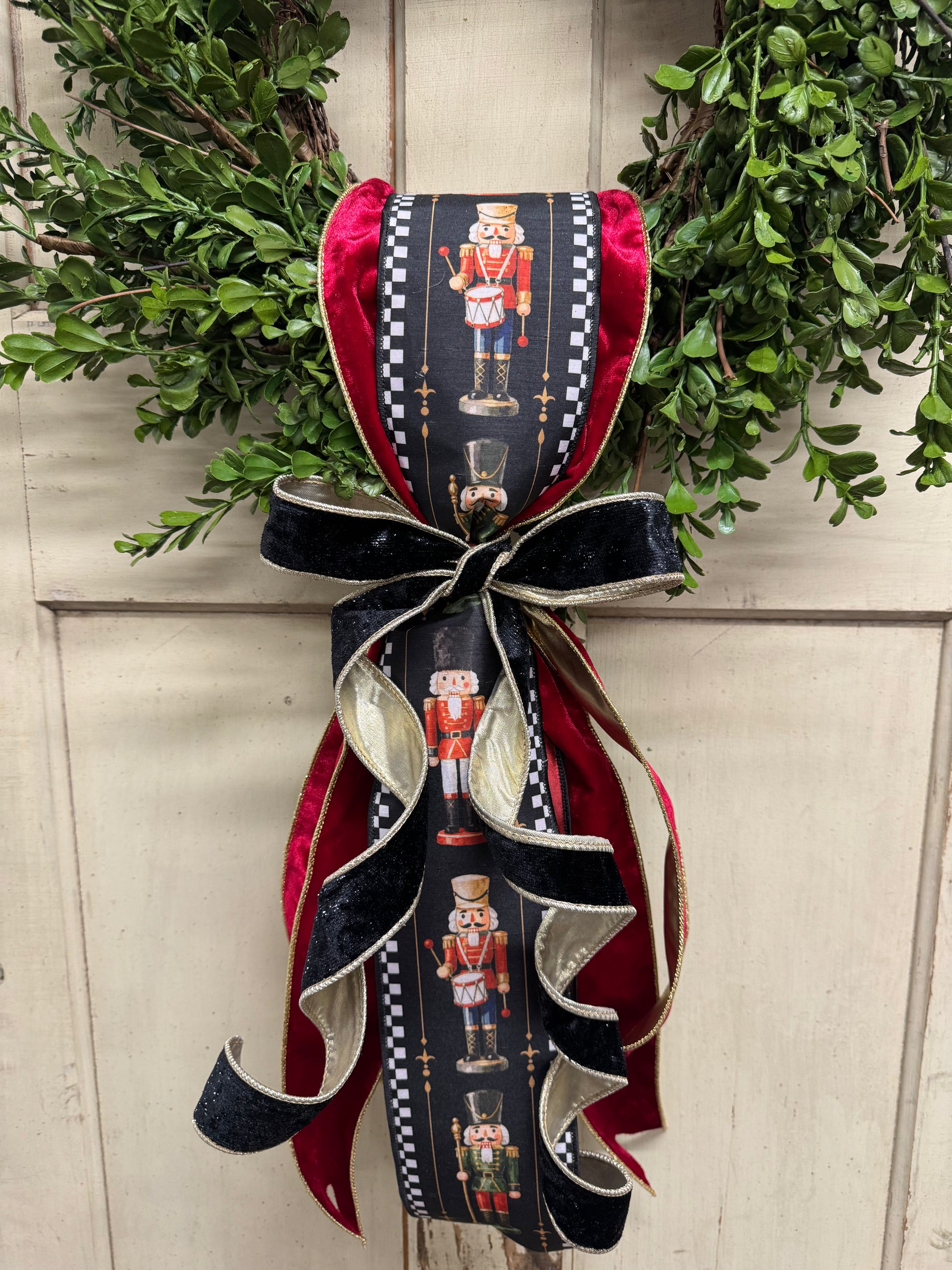 lose up of Nutcracker-print ribbon with black-and-white check borders, layered with red velvet and gold-edged black velvet ribbon on a boxwood wreath.”