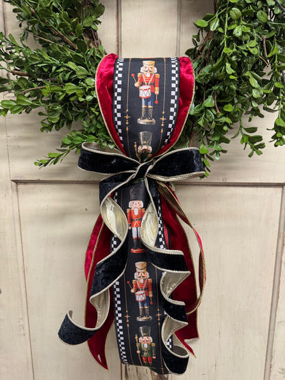 lose up of Nutcracker-print ribbon with black-and-white check borders, layered with red velvet and gold-edged black velvet ribbon on a boxwood wreath.”