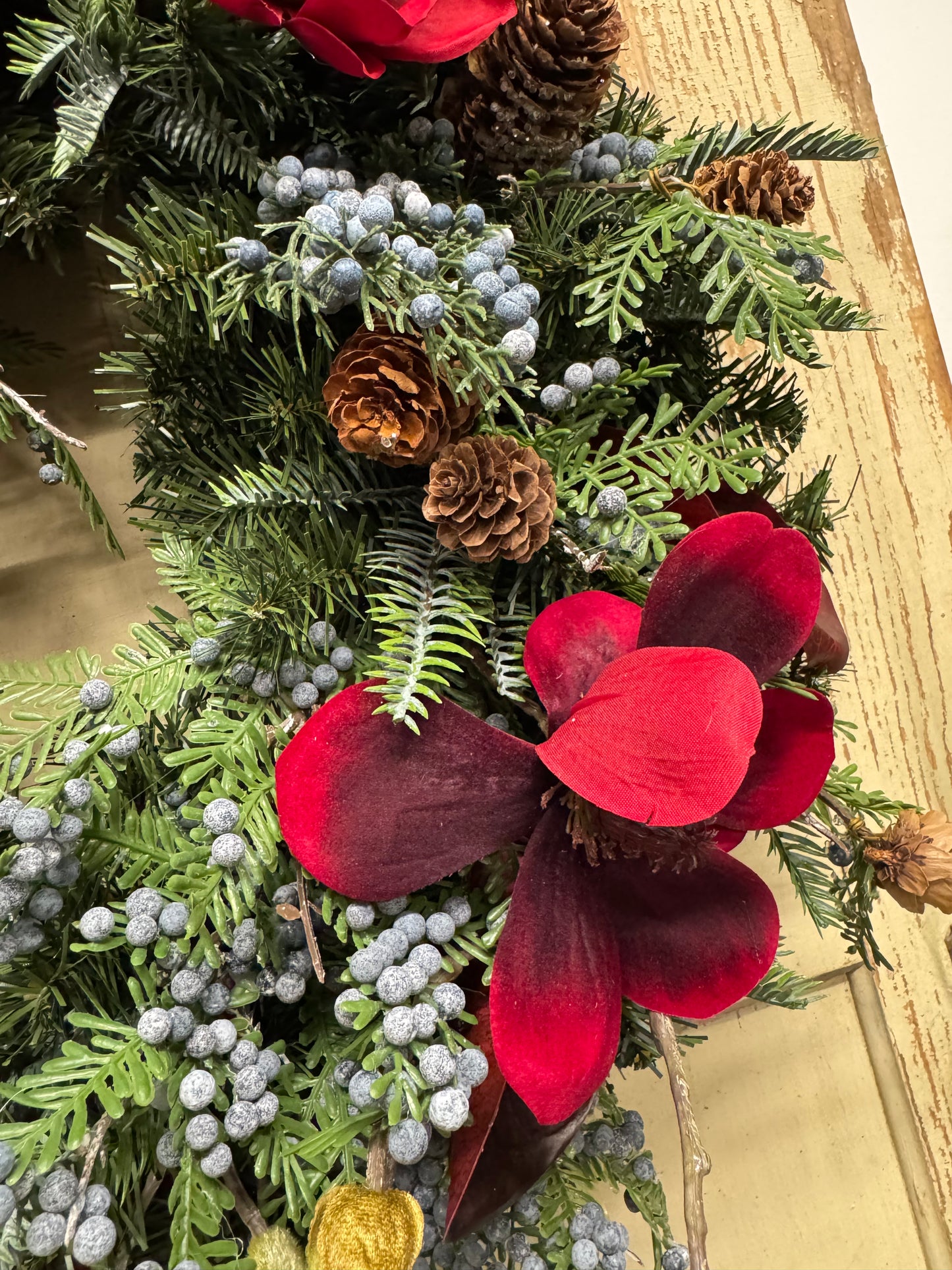 Deep red magnolia flowers with burgundy leaves, dusty blue juniper berries, brown pinecones, and mixed evergreen foliage