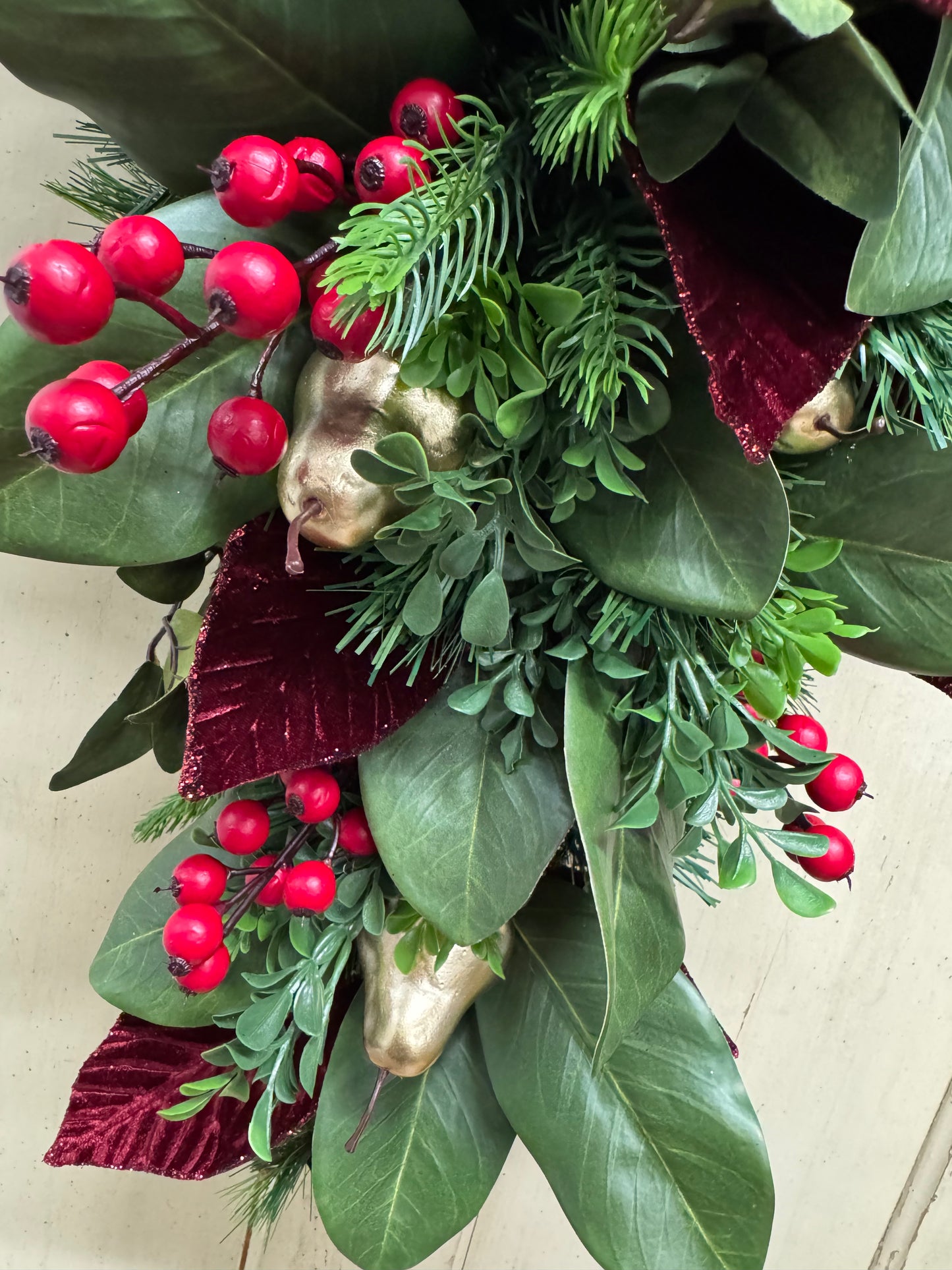 close up Christmas swag detail with red berries, gold pears, green magnolia leaves, pine, boxwood, and burgundy leaves.”