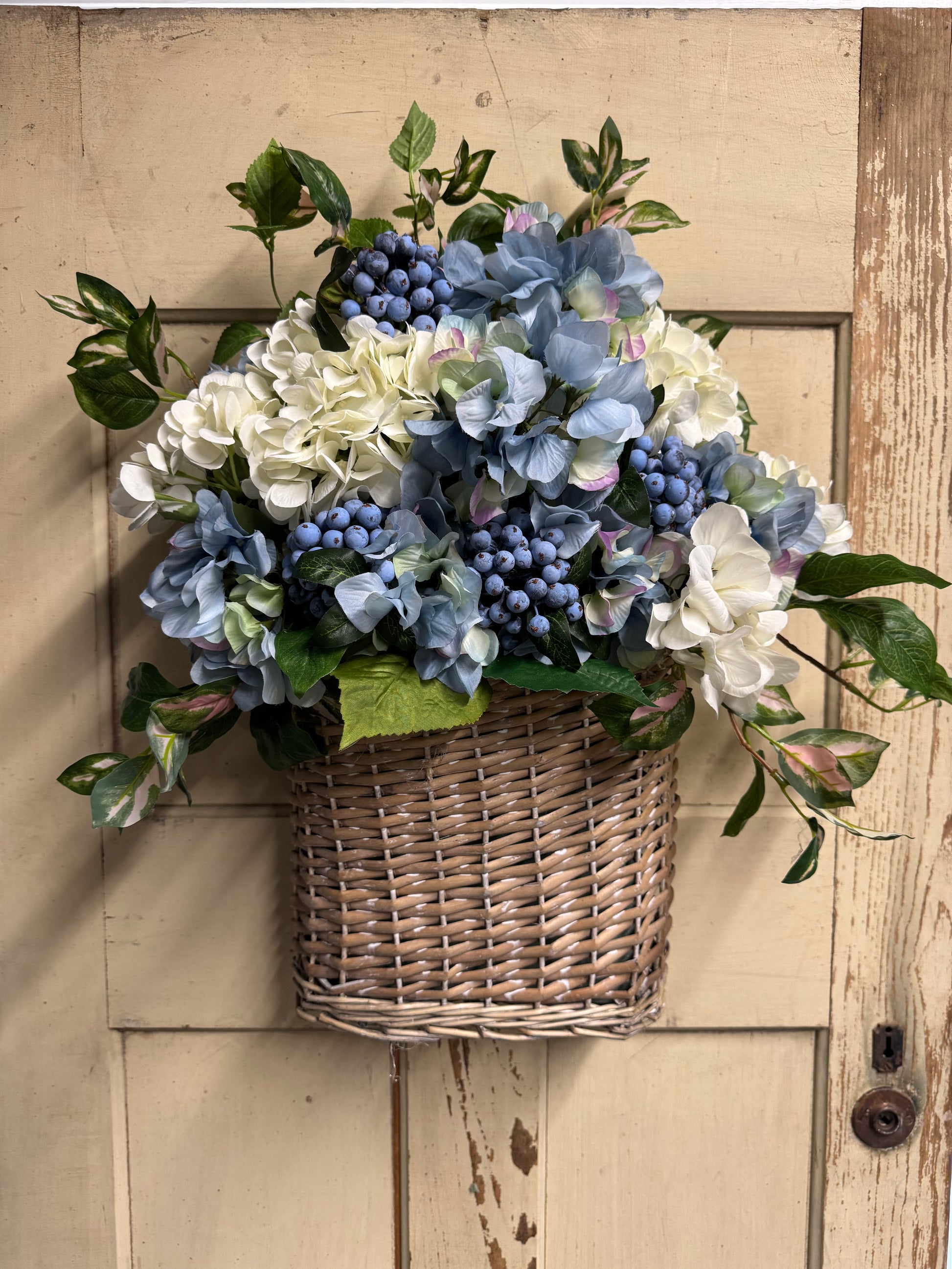 Handcrafted coastal wall basket arrangement with white and blue hydrangeas, blueberry clusters, and Hoya greenery" based on the product details. 