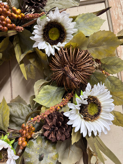 Autumn floral wreath with white daisy-like flowers, brown pinecones, tan leaves, and orange-brown berries on a neutral background.
