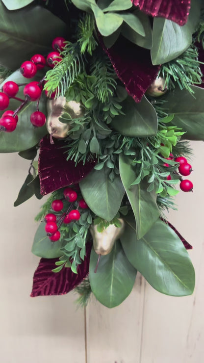 video of Christmas swag detail with red berries, gold pears, green magnolia leaves, pine, boxwood, and burgundy leaves.”