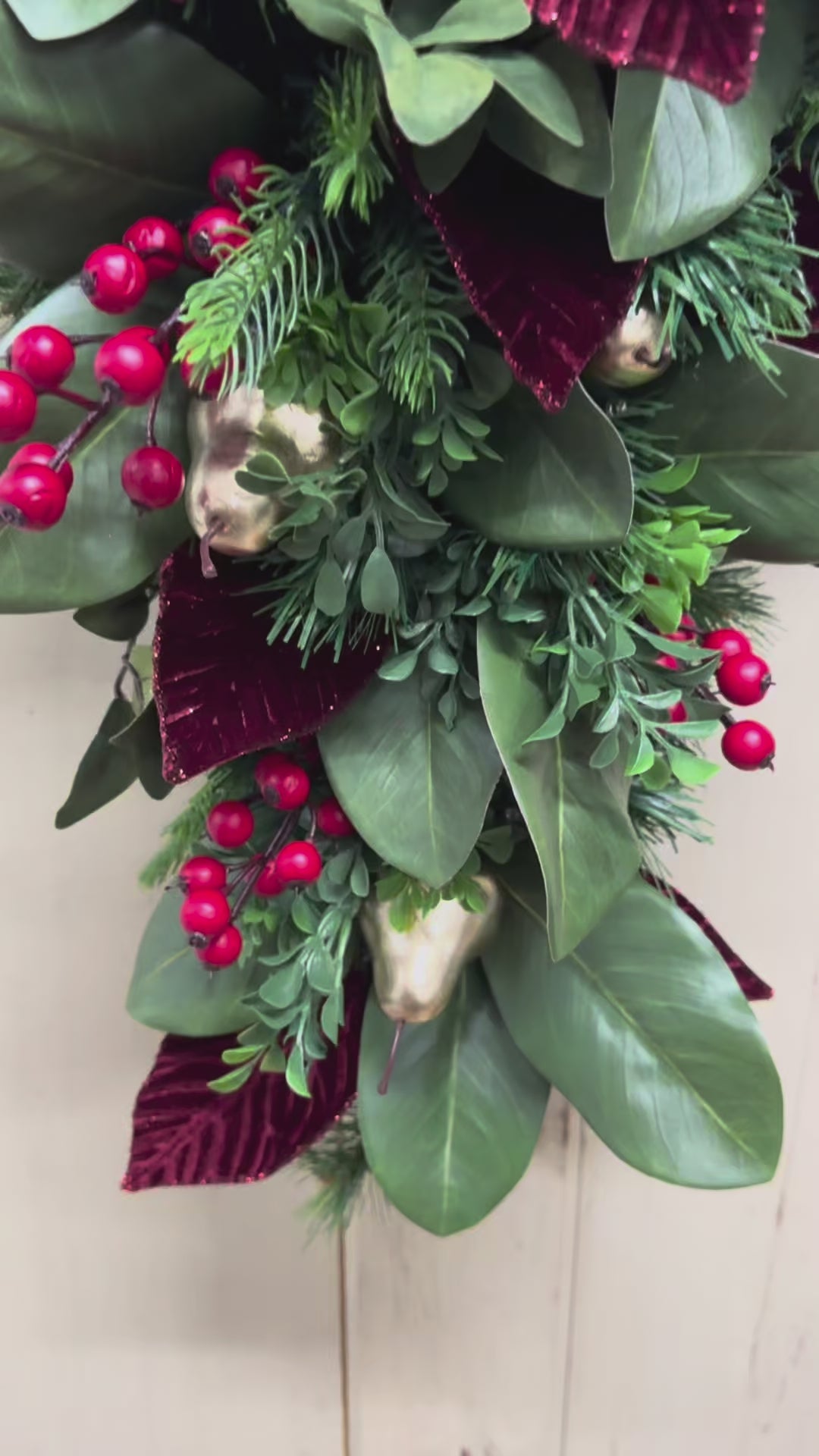 video of Christmas swag detail with red berries, gold pears, green magnolia leaves, pine, boxwood, and burgundy leaves.”