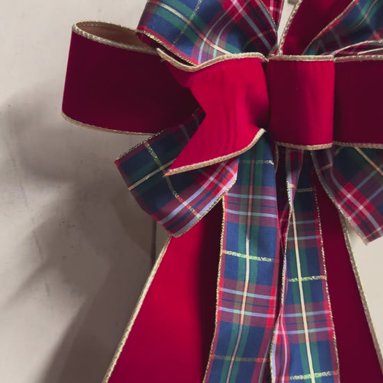 Full view of a layered red velvet and tartan plaid Christmas bow with gold trim, styled against a white shiplap background
