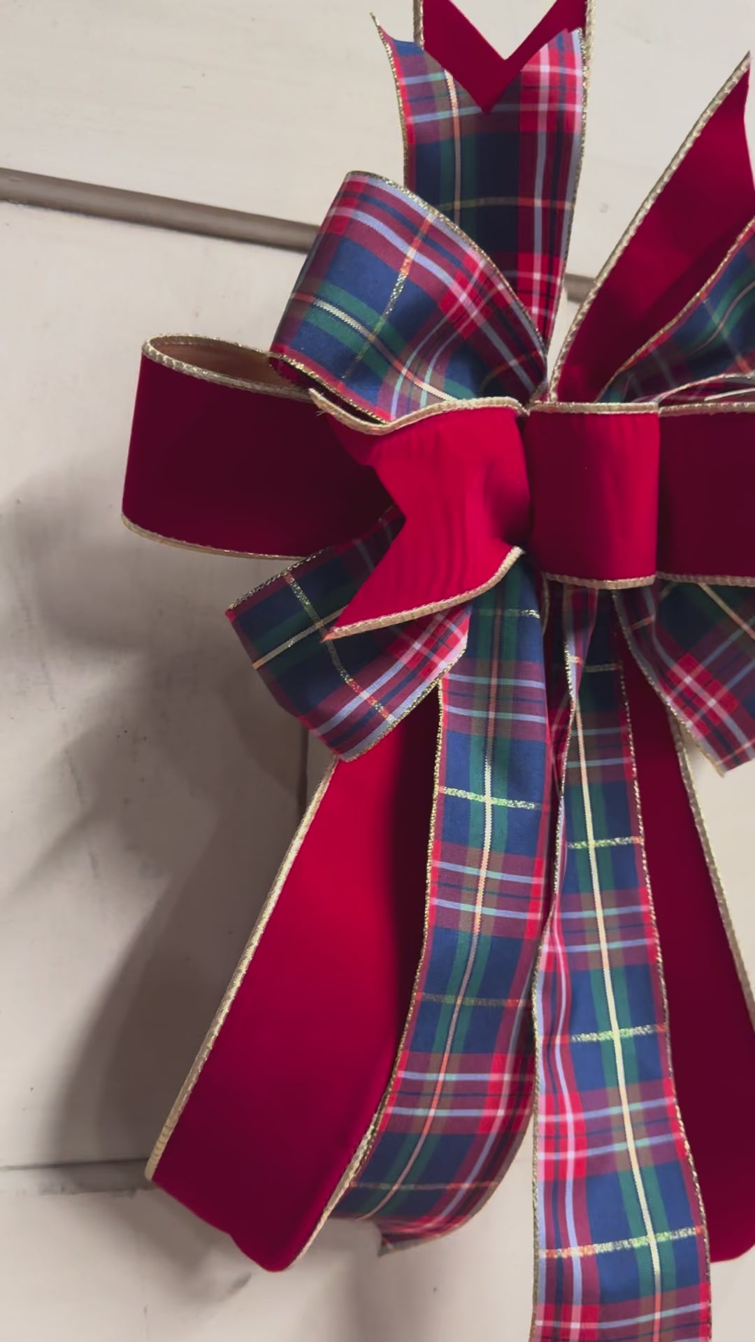 Full view of a layered red velvet and tartan plaid Christmas bow with gold trim, styled against a white shiplap background