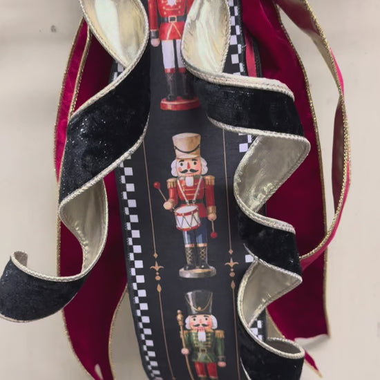 Video of Green boxwood grapevine Christmas wreath with a nutcracker-print ribbon sash, red velvet ribbon, and a gold-edged black velvet bow.”