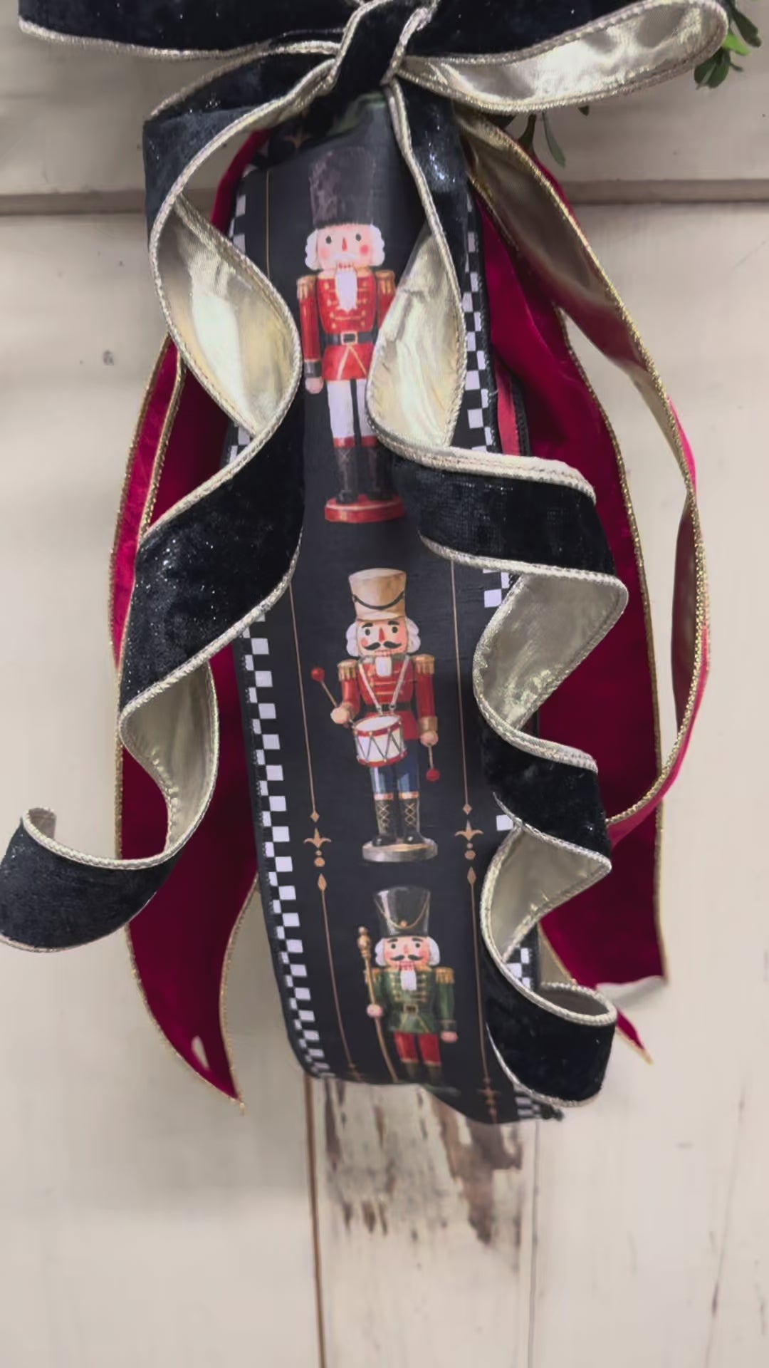 Video of Green boxwood grapevine Christmas wreath with a nutcracker-print ribbon sash, red velvet ribbon, and a gold-edged black velvet bow.”
