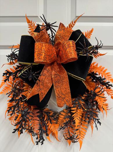 Black and orange handmade Halloween wreath with glitter spiders, orange ferns, and a velvet bow