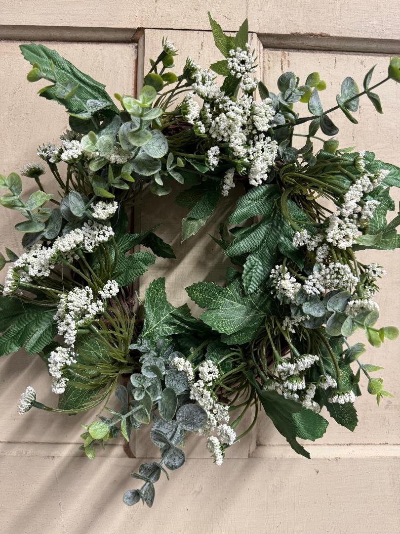 Close-up of Queen Anne lace candle ring showing delicate faux white blooms and green foliage detail, styled around a pillar candle