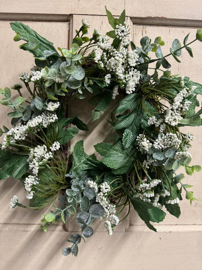 Close-up of Queen Anne lace candle ring showing delicate faux white blooms and green foliage detail, styled around a pillar candle