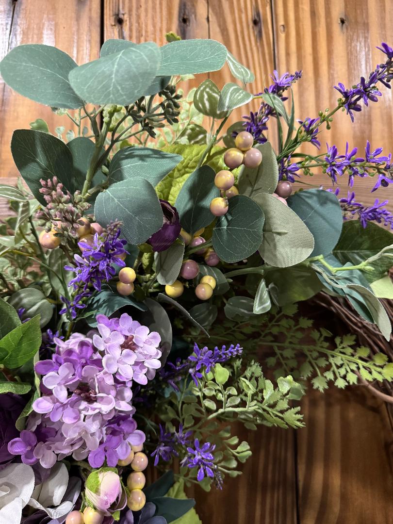 Artificial flower wreath with green leaves, purple flowers, and small yellow berries.