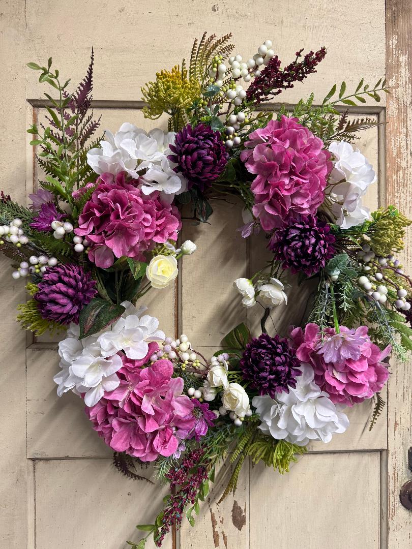 Purple and pink garden wreath with lush faux purple and pink floral blooms and green foliage on a natural base, perfect for front doors and spring home decor"