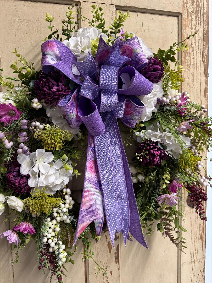 Decorative wreath with purple ribbon and flowers on a wooden door