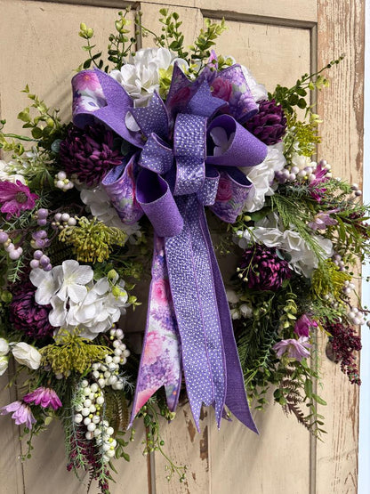 Decorative wreath with purple ribbon and flowers on a wooden door